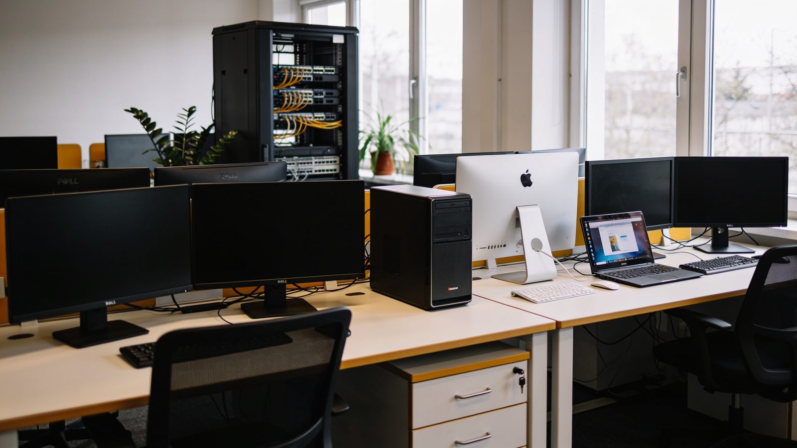 Arbeitsplätze mit Mac und Windows-Rechner, im Hintergrund ein Netzwerkschrank