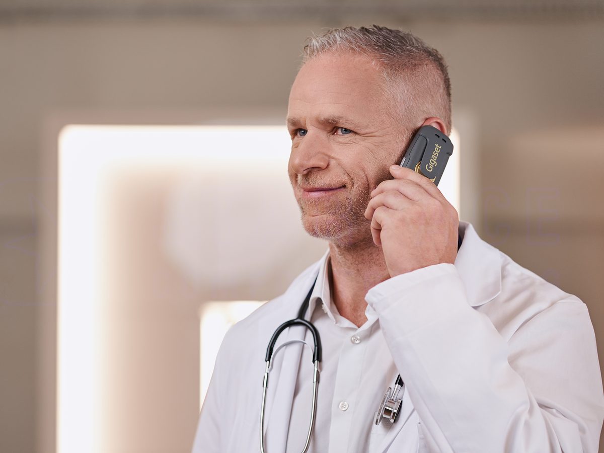 Arzt im Kittel telefoniert mit einem DECT-Mobilteil